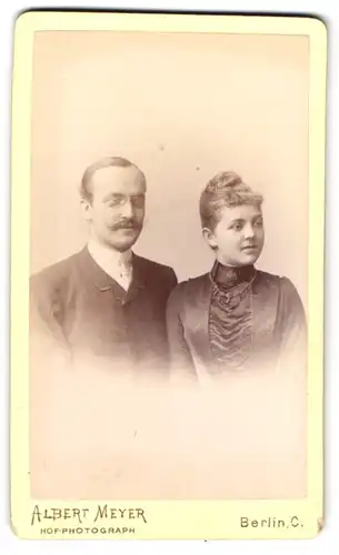 Fotografie Albert Meyer, Berlin, Alexanderstr. 45, Gutbürgerliches Paar in feiner dunkler Kleidung mit Zwicker und Kette