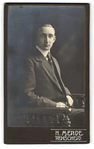 Fotografie H. Mende, Remscheid, Junger feiner Herr im schwarzen Anzug mit Krawatte sitzt entspannt auf einem Stuhl