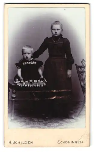 Fotografie H. Schilgen, Schöningen, Zwei junge Geschwister in schwarzen Kleidern mit leicht erstarrten Blicken
