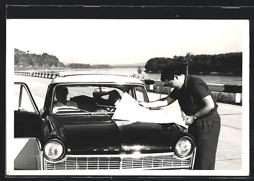 Foto-AK Auto Ford Taunus, Mann schaut auf eine Karte auf der Motorhaube des schwarzen KFZ