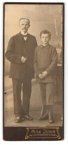 Fotografie Max Jung, Lichtenstein-C. i. S., Knabe im grauen Sakko mit kurzer Hose neben seinem Vater im schwarzen Anzug