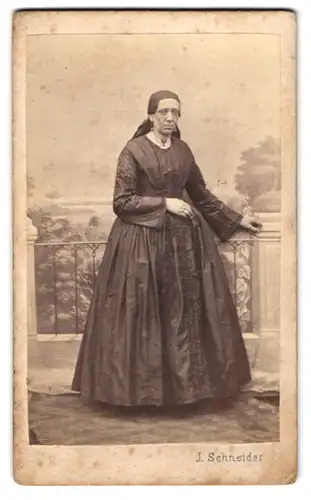 Fotografie J. Schneider, Wien, ältere Dame im dunklen Kleid mit Kopftuch vor einer Studiokulisse