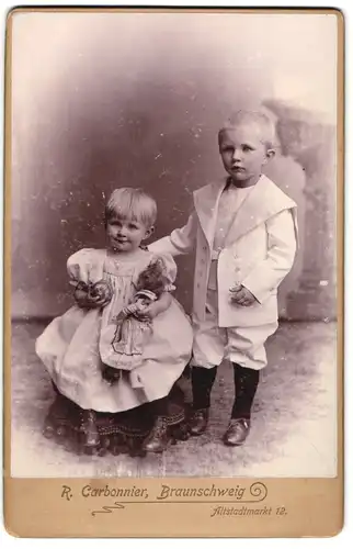 Fotografie R. Carbonnier, Braunschweig, zwei niedliche kleine Kinder im weissen Anzug und im Kleid mit Puppe im Arm