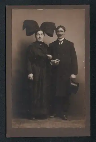 Fotografie unbekannter Fotograf und Ort, Frau im dunklen Trachtenkleid mit Kopfschleife und Herr im Anzug mit Zylinder