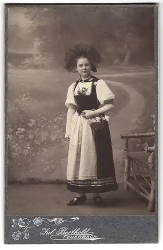 Fotografie Julius Berthold, Feuerbach, junge Frau in Tracht mit Blumenkorb vor einer Studiokulisse, 1906