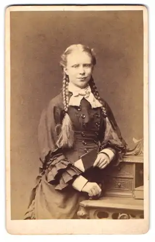 Fotografie E. Bernhard & D. Ebeling, Hamburg, junges blondes Mädchen mit geflochtenen zöpfen am Sekretär stehend