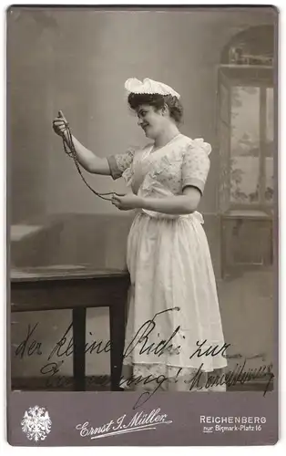 Fotografie Ernst J. Müller, Reichenberg, Schauspielerin im Kostüm betrachtet eine Perlenkette