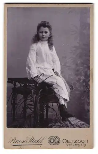 Fotografie Bruno Riedel, Oetzsch bei Leipzig, Junges Mädchen mit lockigem Haar im weissen Kleid auf einem Tisch