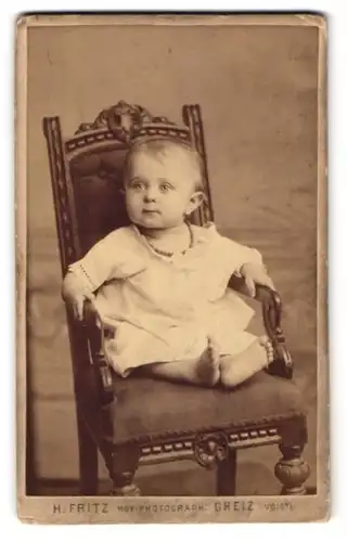 Fotografie H. Fritz, Greiz i. Voigtl., Weststr. 6, Kleinkind im weissen Gewand mit abwesendem Blick auf einem Stuhl