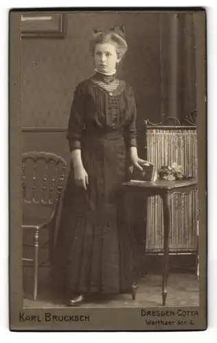 Fotografie Karl Brucksch, Dresden-Cotta, Warthaer Str. 4, Junge Frau in schwarzem Kleid steht an einem Tisch