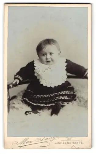 Fotografie Max Jung, Lichtenstein i. S., Schulgasse 3, Lächelndes Baby im Kleid auf einem Fell