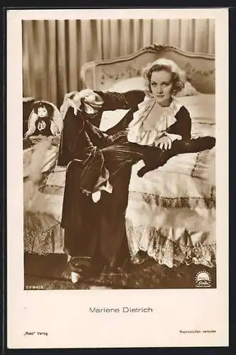 AK Schauspielerin Marlene Dietrich mit Puppe auf einem Bett