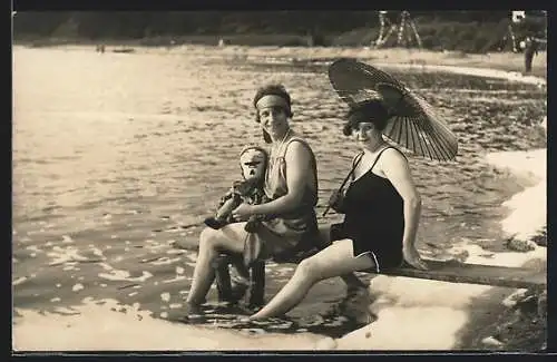 Foto-AK Zwei Frauen in Badeanzügen mit Puppe und Schirm am Wasser