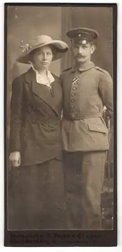 Fotografie J. Fuchs, Charlottenburg, Wilmersdorferstr. 57, Soldat in Feldgrau-Uniform mit Schirmmütze neben Ehefrau