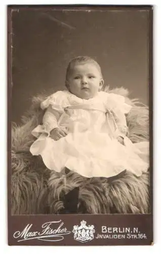 Fotografie Max Fischer, Berlin, Invaliden-Str. 164, Danziger-Str. 98, Süsses Kleinkind im Kleid sitzt auf Fell