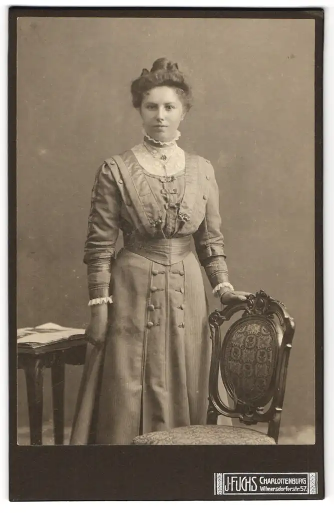 Fotografie J. Fuchs, Charlottenburg, Wilmersdorferstrasse 57, Dame im Kleid neben einem Stuhl