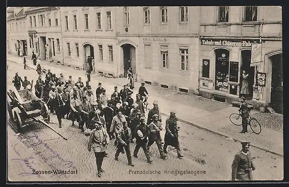 AK Zossen-Wünsdorf, Französische Kriegsgefangene beim Marsch durch eine Strasse, mit Tabakgeschäft