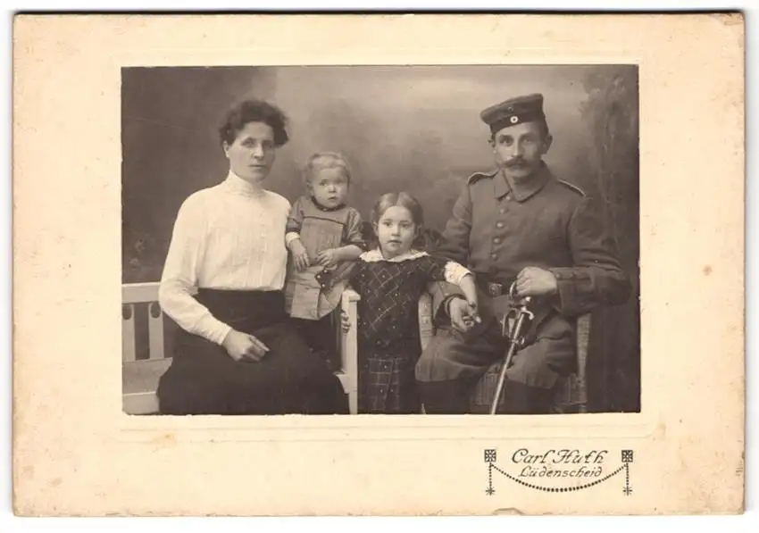 Fotografie Carl Huth, Lüdenscheid, Soldat in Feldgrau-Uniform m. Krätzchen u. Säbel neben Frau u. Kindern