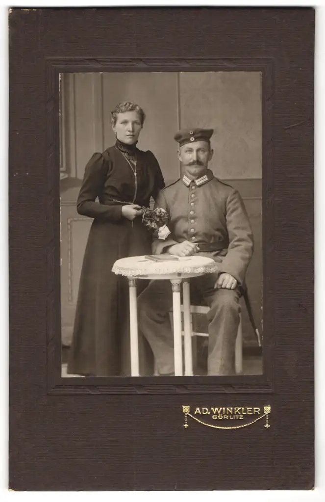 Fotografie A. D. Winkler, Görlitz, Soldat in Uniform mit Kragenspiegel, Krätzchen u. Bajonett neben Ehefrau