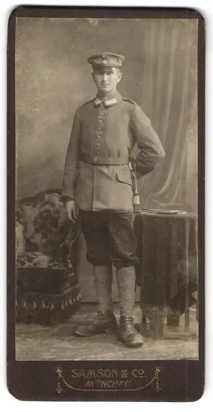Fotografie Samson & Co., München, Neuhauserstr. 7, Soldat in Uniform mit Schirmmütze steht neben Sessel