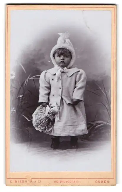Fotografie E. Biegner & Comp., Guben, Am Wilhelmsplatz 9, Kleines Kind im Jäckchen mit Puppe