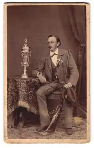 Fotografie Johann Schwarz, Vilshofen, Schützenkönig mit Schützen-Pokal und Scheibenbüchse, 1887