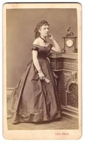 Fotografie Carl Kroh, Wien, attraktive junge Frau im schulterfreien Kleid mit Locken, Kaminuhr