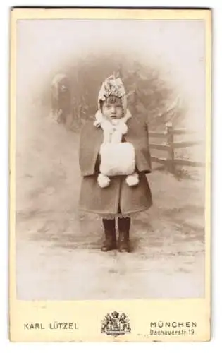 Fotografie Karl Lützel, München, niedliches kleines Mädchen im Winterkleid mit Muff vor einer Studiokulisse Winter