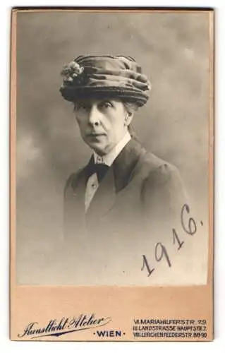 Fotografie Ernst Wiener, Wien, ältere Dame im Blouson mit gerafften Hut samt Blume, 1916