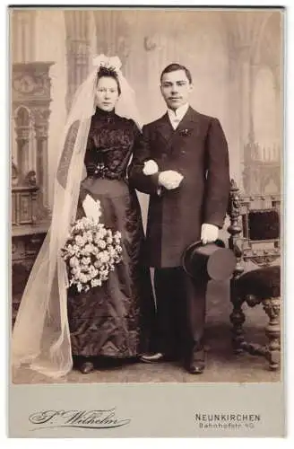 Fotografie J. Wilhelm, Neunkirchen, Bahnhofstr. 40, Junge Braut in schwarzem Hochzeitskleid u. Bräutigam m. Zylinder