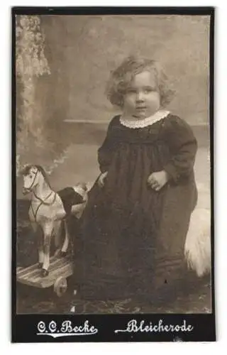 Fotografie C. C. Becke, Bleicherode, Süsses Mädchen m. Locken neben Holzpferd auf Rollen