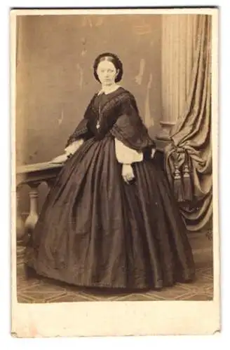 Fotografie unbekannter Fotograf und Ort, junge Frau im schwarzen Reifrock Kleid mit Kette