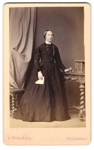 Fotografie L. Strieckling, Oeynhausen, Dame im dunklen Kleid mit Halskette, stehend am Sekretär