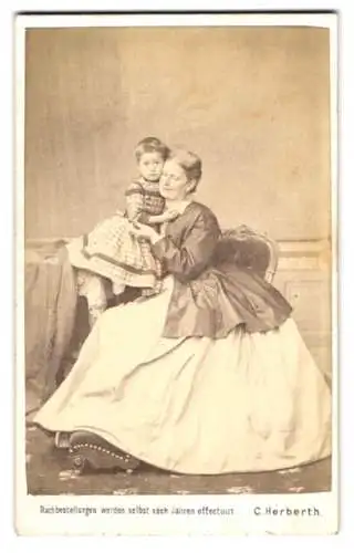 Fotografie C. Herberth, Wieden, Mutter im hellen Reifrock-Kleid mit ihrer Tochter im karierten Kleid auf dem Arm