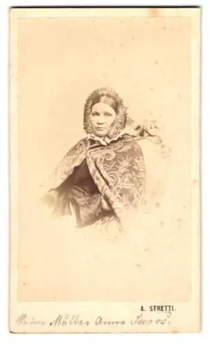 Fotografie A. Stretti, Ort unbekannt, Portrait Frau Anna Saros im Überwurf gehüllt mit Haube