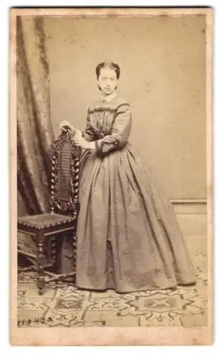 Fotografie J. B. Rottmayer & Co., Graz, hübsche junge Frau im Kleid stehend am Stuhl, Rückseite Zwerg mit Plattenkamera