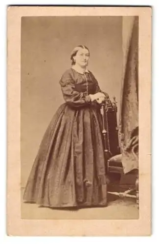 Fotografie unbekannter Fotograf und Ort, Dame im dunklen Kleid posiert stehend am Stuhl