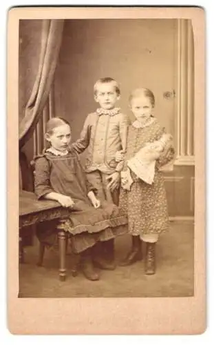 Fotografie Emil Diedrich, Quedlinburg, zwei kleine Mädchen in Kleidern mit Puppe im Arm nebst ihrem Burder