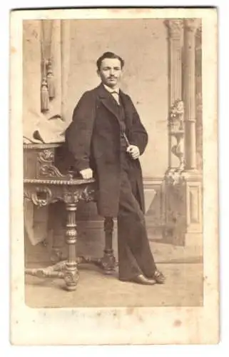 Fotografie Ernst Wolfkamp, Friedeberg Nm., junger Mann im Anzug posiert lässig am Sekretär gelehnt