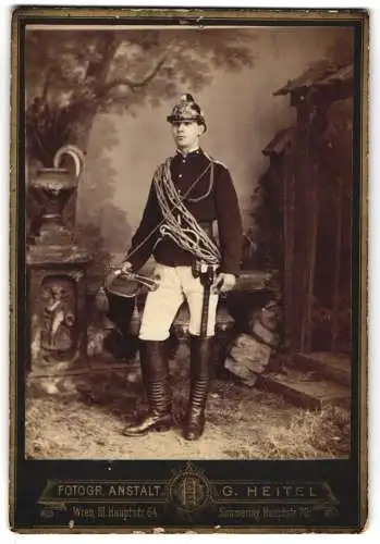 Fotografie G. Heitel, Wien, Hauptstr. 70, junger österreichischer Feuerwehrmann in Uniform mit Helm, Axt und Horn