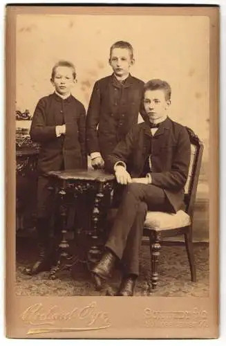 Fotografie Richard Aye, Schwedt a. O., Schlossfreiheit 77, Drei junge Brüder im Anzug an einem kleinen Tisch