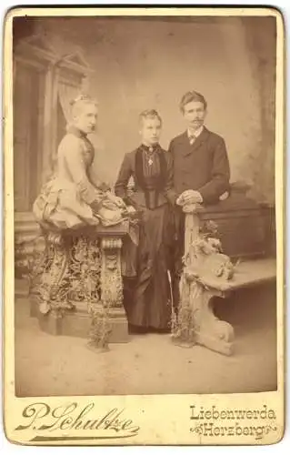 Fotografie P. Schultze, Liebenwerda, Mann nebst zwei Frauen posieren in einer Studiokulisse