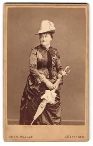 Fotografie Gebr. Noelle, Göttingen, Dame im dunklen bestickten Kleid mit Schirm und Hut
