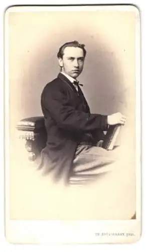Fotografie Th. Brüggemann, Amsterdam, junger Mann im Anzug sitzt verkehrt herum auf einem Stuhl