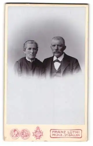 Fotografie Franz Lüthi, Feldle-St. Gallen, Älteres Ehepaar im Sonntagsstaat mit ernsten Blicken