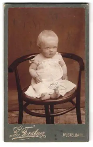 Fotografie L. Forstner, Mistelbach, Wiedenstrasse 6, Blondes Baby im Strampelkleidchen, auf einem Stuhl sitzend