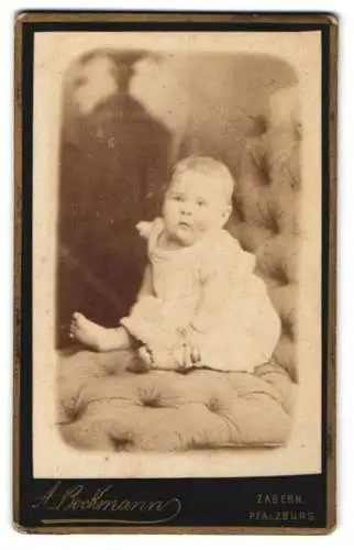 Fotografie A. Bockmann, Zabern, Kleinkind im weissen Kleidchen auf einem Sitzmöbel
