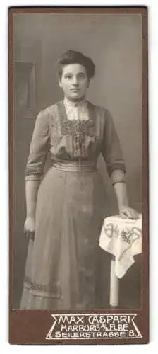 Fotografie Max Caspari, Harburg a. d. Elbe, Seilerstrasse 8, Junge Frau im taillierten Kleid an einem Beistelltisch