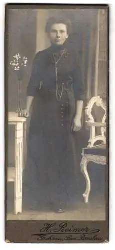 Fotografie H. Reimer, Guhrau /Breslau, Junge Dame im schwarzen Kleid mit Taillengurt mit Quasten, an einem Tisch