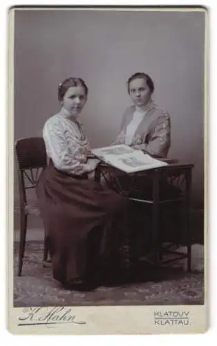 Fotografie K. Hahn, Klattau, Zwei junge Frauen mit einem Bilderbuch am Tisch sitzend